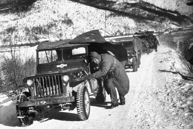 David Douglas Duncan / TIME & LIFE Pictures.U.S. Marine crouching down next to his jeep while leading a convoy of vehicles during the 1st Marine Division's retreat down canyon road they called "Nightmare Alley," after being cut off by the Red Chinese and under fire from nearby hills in December 1950.