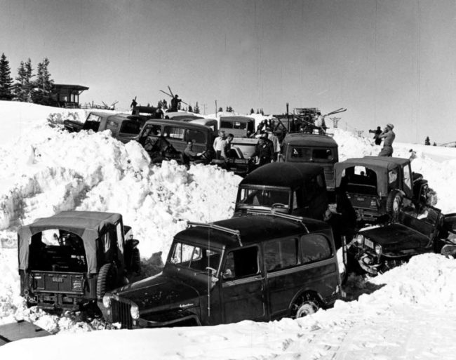 One b/w photograph and negative of about 10-15 jeeps and cars parked up near the top of Aspen Mountain. The Sundeck and lift towers can be seen in the background. There are skiers near the cars getting their equipment out of the cars. Sitting in the jeep is Dave Stapleton, John Thorpe is standing next to him (white shirt, buzz cut), Neil Beck is standing in front of John (grey shirt), and Euclid Worden in black cap. 1954-.